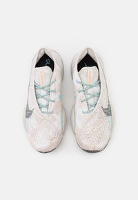 Scarpe sportive chiare con una tomaia in mesh traspirante, lacci turchesi e dettagli a motivo, dotate di una suola ammortizzata per il comfort.