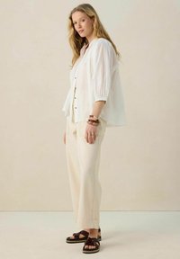 White, button-up, long-sleeve blouse with gathered sleeves, paired with beige wide-leg trousers and brown strappy sandals. Minimalist design.