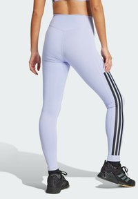 Jasnofioletowe legginsy z czarnymi bocznymi paskami, wysoki stan i elastyczny materiał, w połączeniu z czarnymi butami sportowymi.