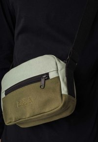 Crossbody tas in mintgroen en olijfgroen canvas. Heeft een voorzak met rits en het 'MELA' logo is op de voorkant gestikt. Zwarte schouderband bevestigd.