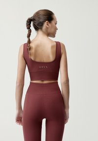 Bordový športový crop top s textúrovanou látkou a širokými ramienkami, kombinovaný s legínami s vysokým pásom, ktoré majú podobný vrúbkovaný dizajn.