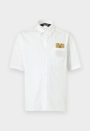 Rövid ujjú fehér ing gallérral, és egy kis színes hímzett folt látható a bal mellzsebben.