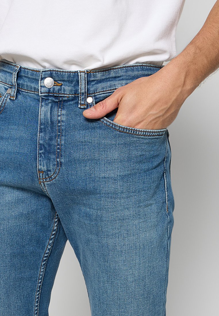 Jean en denim dans un délavage bleu clair avec un design à jambe droite, featuring des éléments en métal argenté, une fermeture à bouton et une poche avant.