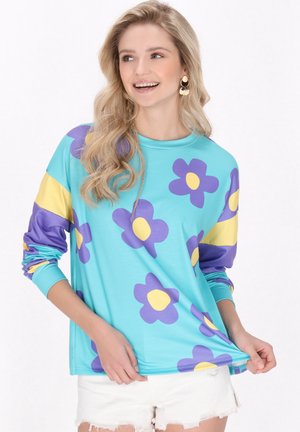 Camicia a maniche lunghe in tessuto turchese decorata con grandi fiori viola e centri gialli. Presenta maniche a righe gialle e viola.
