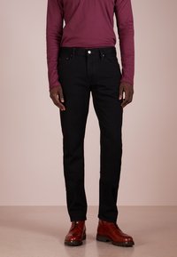 Schwarze Denim-Jeans mit geradem Schnitt, kombiniert mit einem bordeauxfarbenen Langarmhemd und braunen Lederstiefeln mit strukturierter Oberfläche.