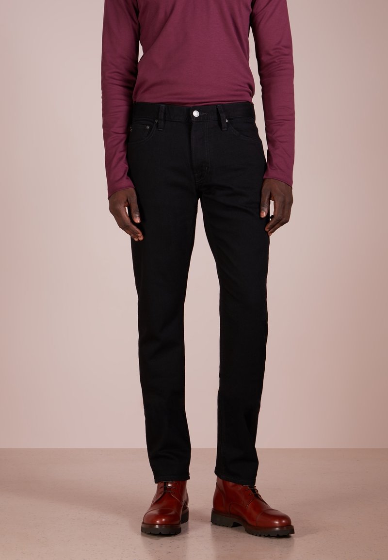 Schwarze Denim-Jeans mit geradem Schnitt, kombiniert mit einem bordeauxfarbenen Langarmhemd und braunen Lederstiefeln mit strukturierter Oberfläche.