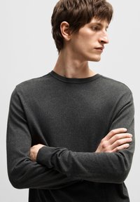 Dark gray, long-sleeve sweater with a crew neckline. Soft texture and fitted design, featuring ribbed cuffs and a relaxed silhouette.