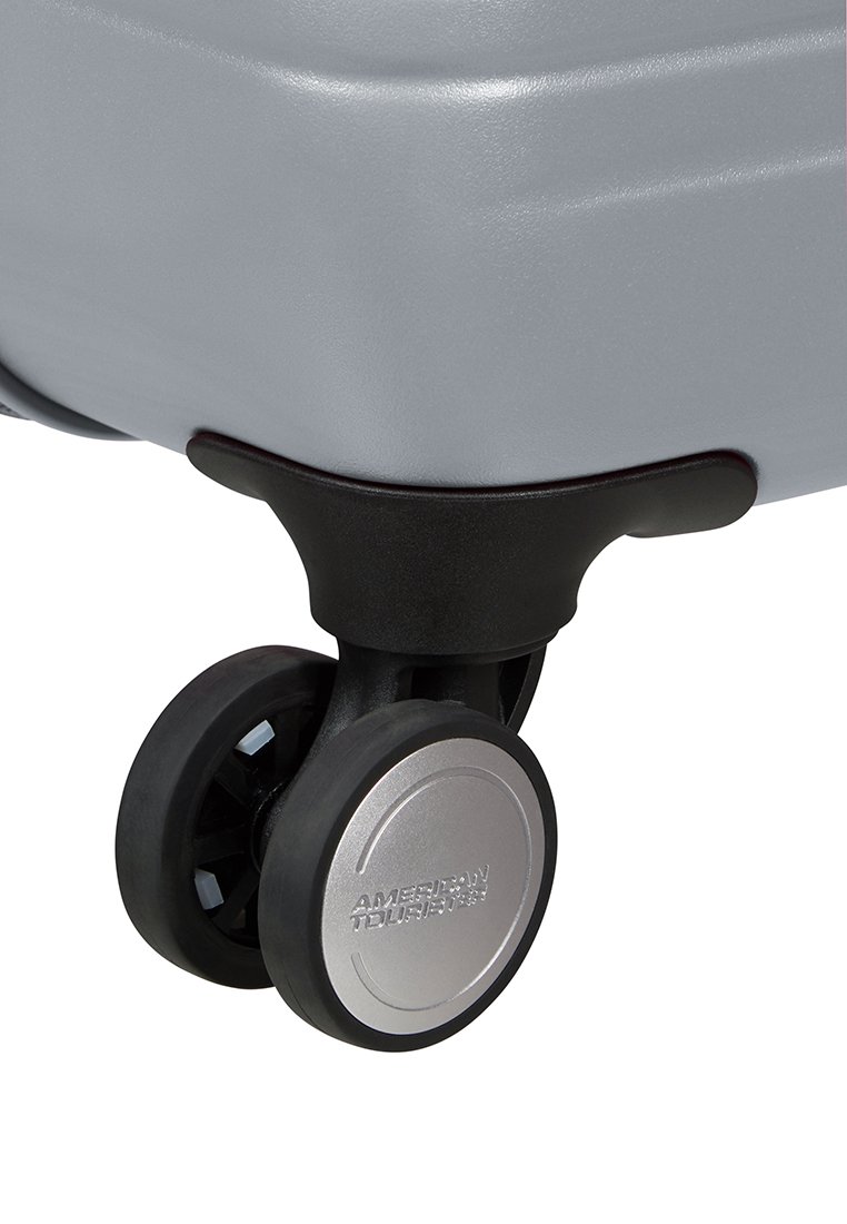 Esquina de una maleta rígida plateada con un acento de plástico negro y cuatro ruedas giratorias dobles con un centro metálico plateado que presenta la marca.