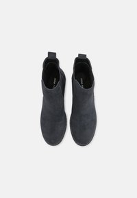 Bottes cheville en daim noir à texture lisse, bout arrondi, languette de traction à l'arrière et détails de couture minimalistes autour de la semelle.