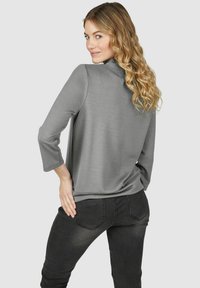 Grijze langekleurige top met een ontspannen pasvorm, voorzien van een ronde halslijn en subtiele glans. Gemaakt in combinatie met strakke zwarte jeans.