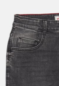 Jean en denim gris foncé, avec un design classique à cinq poches, un léger délavage et un accent de couture rouge le long de la ceinture.