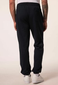 Marine joggerbroek met een elastische tailleband, taps toelopende pijpen en een achterzak, gecombineerd met witte sneakers. Zachte textuur.