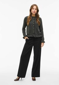 Siv svileni kardigan z nabranimi robovi in dekorativnimi gumbi, kombiniran z visokim črnim širokim hlačami in rjavimi čevlji s peto.