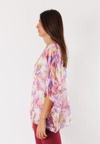 Top leggero e trasparente in stile kimono con stampa floreale multicolore in viola, rosa e giallo. Presenta maniche ampie e una vestibilità morbida.