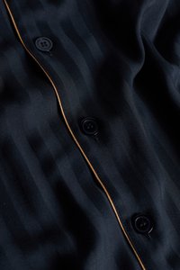 Námořnická košile na knoflíky s jemnými vertikálními pruhy, hladkou texturou, černými knoflíky a kontrastním béžovým lemováním podél zapínání.