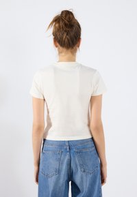 Kortermet kremfarget bomull t-skjorte med rund hals, kombinert med høyt midje blå denim jeans med baklommene og en avslappet passform.