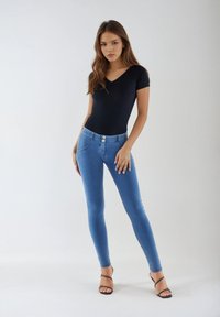 Siniset kapeat farkut, joissa on kaksi etutaskua ja nappikiinnitys, yhdistetty mustaan V-aukkoinen bodysuitiin ja mustiin remmikenkiin.