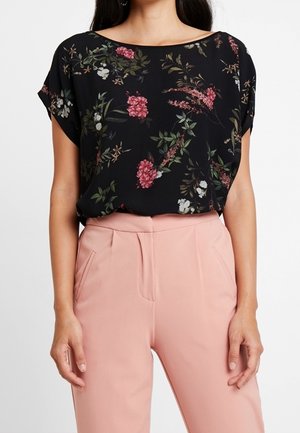 Blomster-bluse med korte ærmer i sort med røde og hvide blomster; løs pasform og rund halsudskæring, parret med lyserøde skræddersyede bukser.