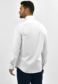 Witte blouse met lange mouwen en een klassieke kraag, gladde textuur, afgeronde zoom en met knopen gesloten manchetten. Gekocht met donkere broek.