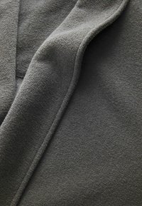 Prizor od blizu mehke, temno sive tkanine z vidnimi gubami in teksturirano, rahlo dvignjeno površino.