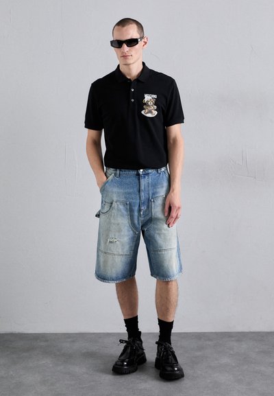 Svart polo tröja med björnlogo, ihop med bleka blå jeansshorts med fickor och slitna detaljer. Svarta strumpor och skor.