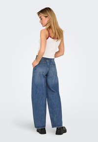 Jeans in denim a gamba larga di colore blu medio, con vita alta, due tasche posteriori e una vestibilità comoda. Abbinati a un top bianco.