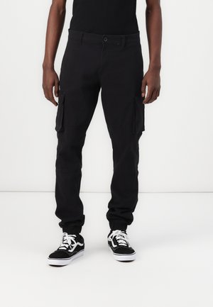 Black cargo pants with side pockets, tapered cuffs, button closure, and a smooth fabric texture, paired with black and white sneakers.