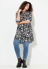 Tunica floreale nera, con fiori viola e bianchi, abbinata a jeans azzurri chiari e stivaletti neri. Maniche arrotolate e orlo asimmetrico.