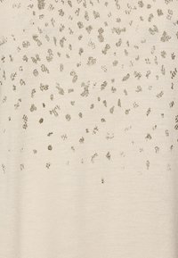 Bežová tkanina s texturovaným vzorem metalických zlatých teček různých velikostí, vytvářející rozptýlený efekt po celé ploše.