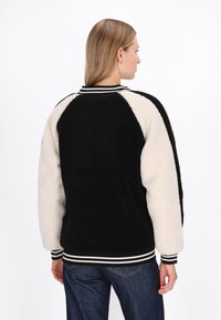 Sort og creme fleecejakke med ribbet krave, stribede ærmer og afslappet pasform, med kontrastærmer og tekstureret stof.