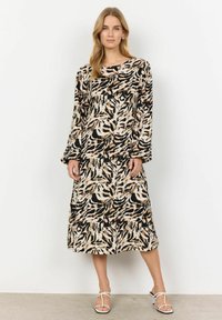 Mekko, jossa on pitkät hihat, musta ja beige lehtikuosi, löysä istuvuus ja pyöreä kaula-aukko, ulottuen puoliväliin pohkeita.