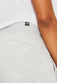 Grå sweatpants med ribbet talje og ekstern logoetiket. Stoffet har en blød tekstur og synlige sømdetaljer.