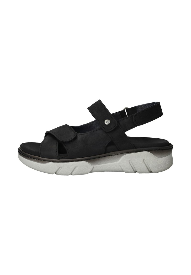 Sandale en suède noir avec un design à bout ouvert, une bande ajustable et une semelle en caoutchouc blanc avec un motif texturé.