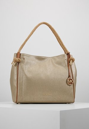 Sac à main Michael Kors beige texturé avec poignées en corde tressée, breloque logo dorée et design minimaliste sur un piédestal blanc.