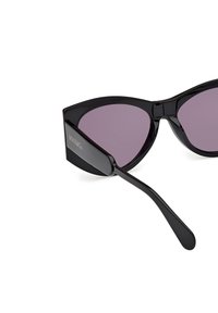 Gafas de sol negras con forma de ojo de gato y lentes de un púrpura oscuro. Fabricadas en plástico brillante, presentan una forma curvada y patillas elegantes. Detalle del logo grabado.