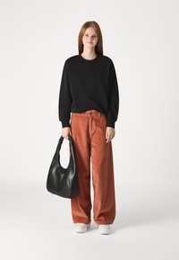 Black crewneck sweatshirt, orange corduroy wide-leg pants, white sneakers, and a black hobo bag. Simple design and smooth textures.