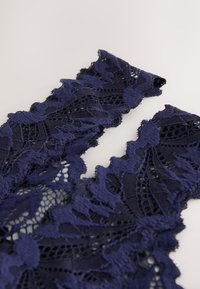 Marineblåt blonderstof med indviklede blomsterdekorationer og teksturerede kanter, med åbne vævninger og bløde, delikate tråde.