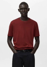 Czerwona bawełniana koszulka z okrągłym dekoltem i krótkimi rękawami, zestawiona z ciemnymi dżinsami. Gładka faktura, prosty krój i standardowe dopasowanie.