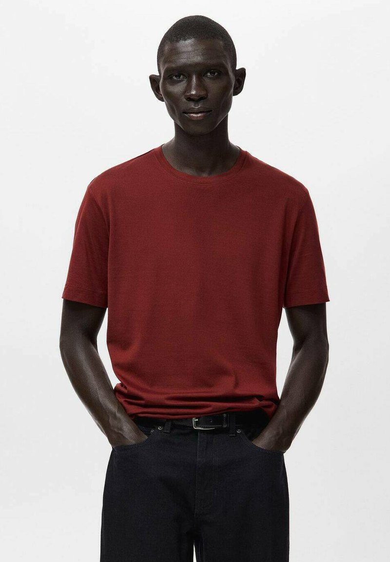 Czerwona bawełniana koszulka z okrągłym dekoltem i krótkimi rękawami, zestawiona z ciemnymi dżinsami. Gładka faktura, prosty krój i standardowe dopasowanie.