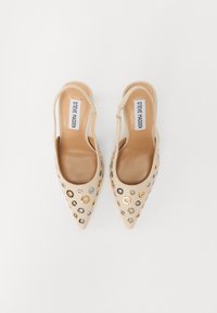 Beige slingback shoes featuring pointed toes, a smooth leather texture, and decorative metal grommets in gold, silver, and black.