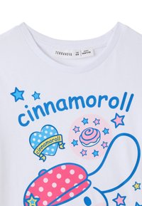 T-shirt bianca in cotone con un personaggio dei cartoni animati dai dettagli blu, cappellino a pois rosa e stelle e cuori colorati. Marca: Terranova.