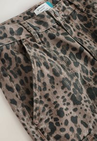 Jeans o prostym kroju, wysokiej talii, w brązowym materiale z zielonym wzorem zwierzęcym. Cechują się widocznym szwem i metalowym zapięciem.