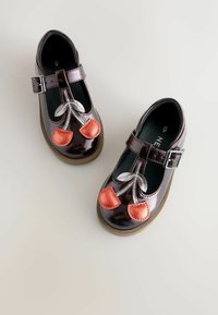 Braune Lacklederschuhe mit T-Riemen, verziert mit roten Kirschen-Applikationen und silbernen Akzenten an der Vorderseite. Mit Schnallenverschluss und runder Zehenform.