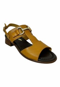 Sandalia de cuero marrón con diseño de barra en T, correa de tobillo ajustable y detalle de hebilla metálica. Presenta un tacón bajo y punta abierta.