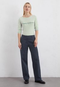Camicia a maniche lunghe a righe verde e bianca con scollatura tonda. Abbinata a pantaloni larghi blu scuro e scarpe nere.