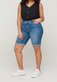 Shorts en denim avec un ourlet effiloché, de couleur bleu clair, au design ajusté et au style à cinq poches. Associés à un top sans manches noir et des baskets blanches.