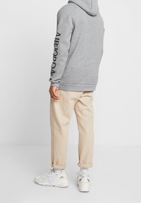 Sudadera gris con el texto negro "AIR JORDAN" en la manga, combinada con pantalones beiges y zapatillas blancas. Diseñada para un ajuste cómodo.
