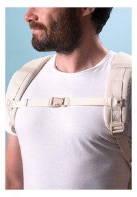 Beige chest strap system featuring adjustable padded shoulder straps and a plastic buckle, worn over a white shirt, with a neutral background.