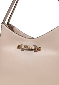 Borsa a tracolla in pelle beige con una texture liscia, dotata di una chiusura con logo dorato e doppie spalline sottili.