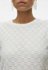 Top bianco e texturizzato con un motivo floreale. Il design presenta un collo tondo ed è abbinato a grandi orecchini rotondi.